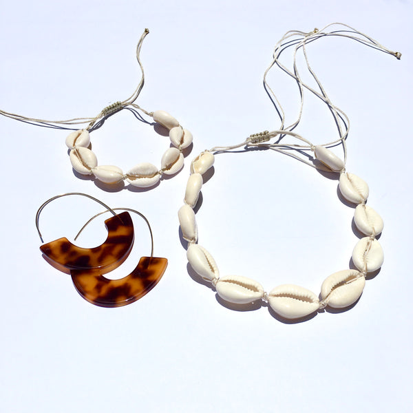 WHITE COWRIE SHELL BRACELET AND NECKLACE STRUNG ON A NATURAL COLORED CORD AND EASY KNOT CLOSURE FOR ADJUSTING THE LENGTH. GREAT PIECES FOR SUMMER AND VERY LIGHT AND EASY TO WEAR. ALSO SHOWN ARE TURTLE SHELL HALF HOOP ACRYLIC HOOK EARINGS. GREAT EARRINGS